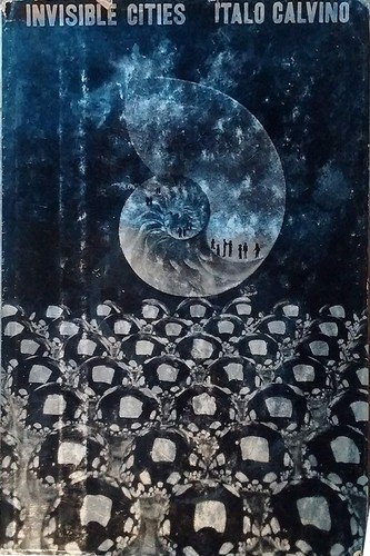 Cover of a hardcover edition of Invisible Cities by Italo Calvino, a dark blue jacket showing a spiraling nautilus shell against a starfield, with tiny silhouetted figures walking along its curve above a field of stone rooftops